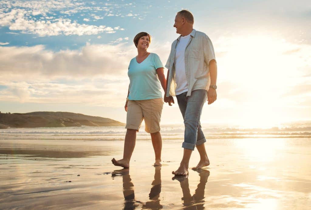 mature couple holding hands while walking on the beach. Carefree and happy after getting their estate plan finalized.